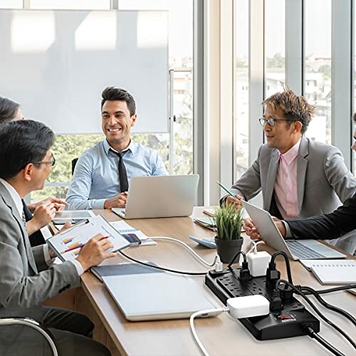Office meeting with people using laptops and a power strip on the table.