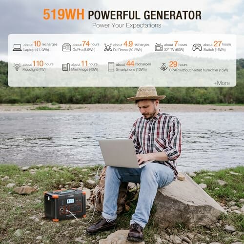 Man using a laptop by a river with a portable generator beside him.