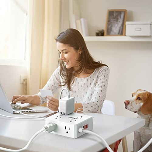 Woman working on laptop at table with dog and power strip.